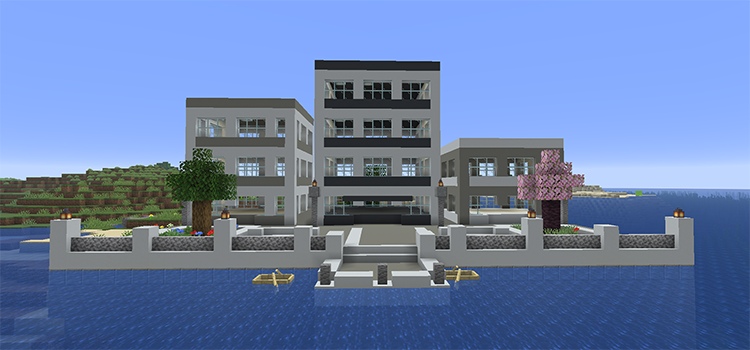 White concrete city promenade over the ocean with tree planters, railings, steps down to the water and modern buildings behind