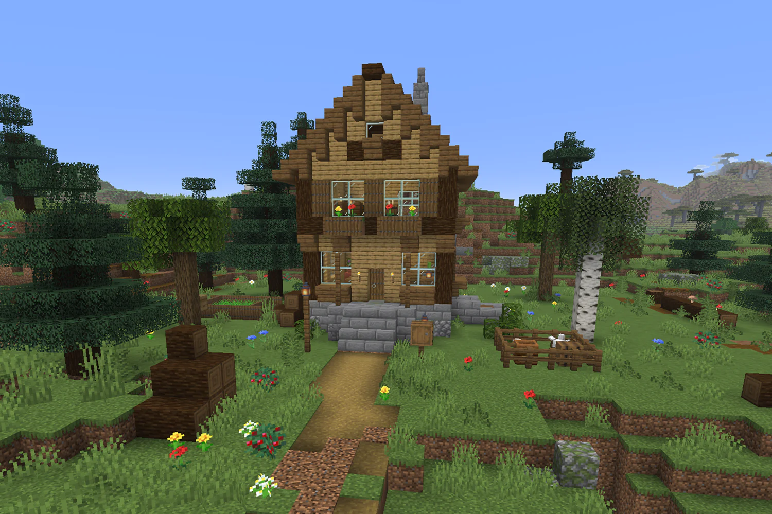 Small multilevel wooden Minecraft house with a stone basement, second floor with flower boxes, steep roof, outside cellar door, and chicken pen in the yard
